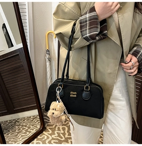 Detail einer schwarzen Leder-Schultertasche mit goldenen Beschlägen und Plüschbär-Anhänger