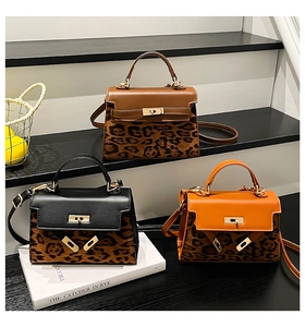 Three leopard print kelly bags in black, brown, and orange displayed on tiered stands