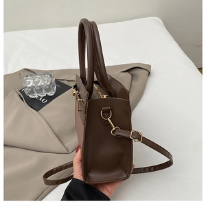 Détail du sac en cuir marron foncé avec texture tressée et boucle en métal doré