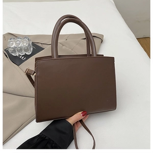Gros plan d'un sac à main marron avec poignées cylindriques et texture en cuir synthétique mat
