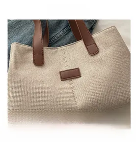 Detail view of woven beige canvas tote bag with brown leather handles and decorative patch