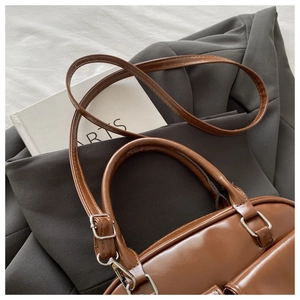 Detail of brown glossy leather handbag showing adjustable strap and metal hardware