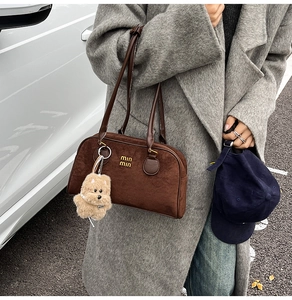 Detailansicht einer braunen Wildledertasche mit Goldlogo und flauschigem Hundeanhänger