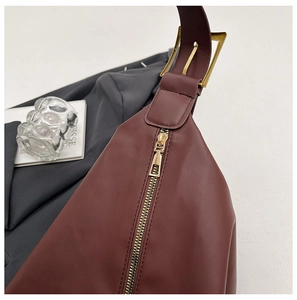 Detailed close-up of golden zipper and smooth burgundy leather texture on a shoulder bag