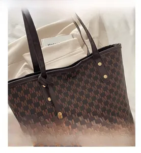 Close-up of brown monogram tote bag with gold M pendant and leather shoulder strap detail