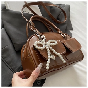 Detail of glossy brown Boston bag featuring dual front pockets and pearl bow charm
