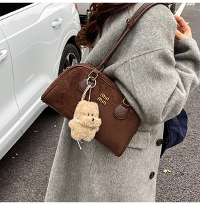Detail einer braunen Wildleder-Bowlingtasche mit Plüschhund-Anhänger am Leder-Schultergurt