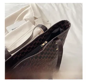 Close-up of smooth gold metal zipper and Monogram pattern on brown leather tote bag