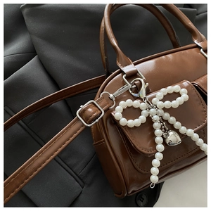 Close-up of brown PU leather bag with pearl bow charm and silver buckle detail
