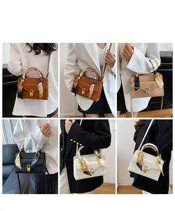 Detail of elegant square handbag with golden oval clasp and decorative floral scarf on handle