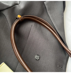 Details des braunen Lederriemens mit Goldbeschlägen auf grauem Blazer-Hintergrund