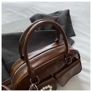 Detail view of glossy brown Boston bag with pearl side pocket and dual zippers