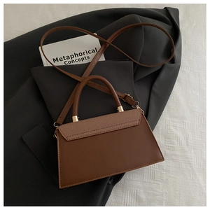 Detail of a brown trapezoid crossbody bag with textured fabric flap and gold hardware