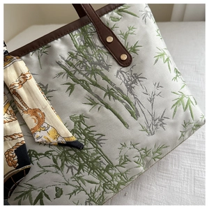 Detailed macro view of green bamboo embroidery and brown leather handles on the tote bag
