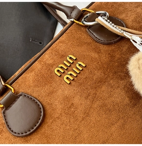 Detailaufnahme der braunen Wildlederstruktur mit Metalllogo und Lederbesatz der Tasche