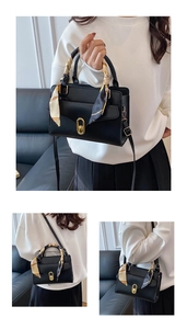 Detail of black faux leather handbag with silk scarf handle and gold oval turn-lock clasp