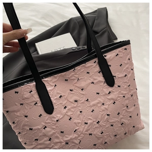 Detail of pink quilted tote bag with black bow patterns and elegant long shoulder straps