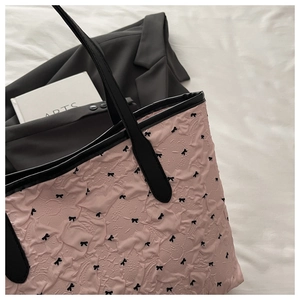 Detail of pink bubble texture tote bag featuring black bow patterns and slim handles