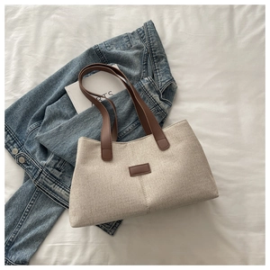 Detailed shot of beige textured fabric tote with dark brown leather handles on white fabric