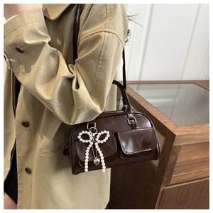 Detail of dark brown glossy Boston bag with pearl bow charm and flap pockets