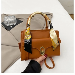 Détail d'un sac en cuir caramel avec poignée foulard en soie et fermoir doré