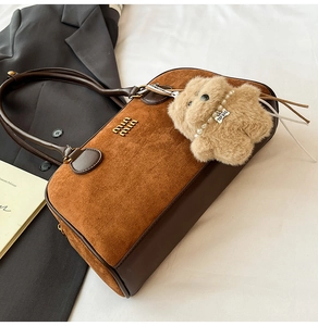 Detailansicht der braunen Wildledertasche mit goldenem Logo und Plüsch-Hundeanhänger