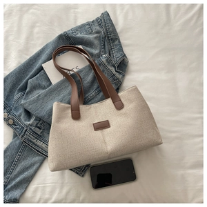 Flat lay of linen tote bag with brown leather handles and center patch on white background