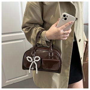 Detail of glossy brown patent leather handbag with pearl bow charm and side pockets