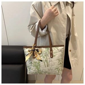 Detail of a beige tote bag featuring green bamboo patterns and a silk scarf on the handle