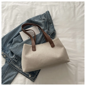 Flat lay of cream canvas tote bag with brown leather handles and casual denim jacket