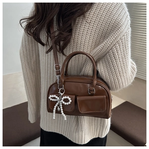 Detail of dark brown glossy bowling bag featuring double pockets and pearl bow charm