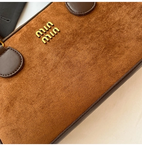 Detaillierte Nahaufnahme der braunen Wildlederstruktur mit Metall-Designer-Logo auf der Tasche