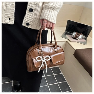 Detail of a brown glossy leather Boston bag featuring front pockets and pearl bow charm