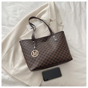Détail d'un cabas monogramme marron avec breloque logo M dorée sur un blazer blanc