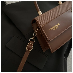 Detail of brown leather bag featuring woven fabric patchwork and gold metal hardware