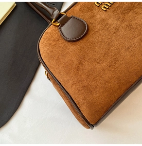 Detailaufnahme der braunen Wildlederstruktur und des goldenen Metalllogos der Tasche