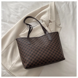 Close-up of brown tote bag with M letter monogram on beige suit and white fabric