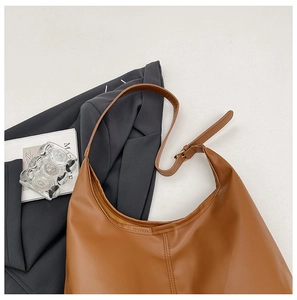 Close-up of caramel hobo bag with vertical stitching and adjustable strap on a gray background
