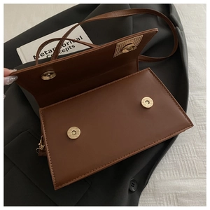 Detail view of brown crossbody bag with double magnetic snaps and golden hardware texture