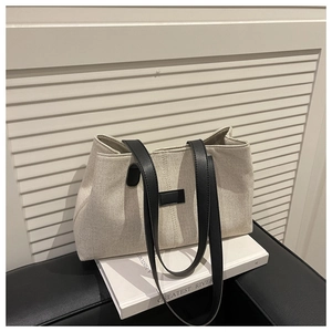 Detail view of beige canvas tote bag with black leather straps on minimalist background