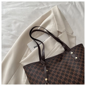 Gros plan d'un sac cabas marron avec motif M et rivets dorés sur une veste chic