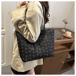 Detail of black tote bag featuring pleated fabric and white bow patterns with long handles