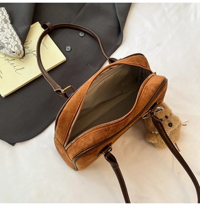 Nahaufnahme der braunen Wildleder-Bowlingtasche mit Goldreißverschluss und Bärenanhänger