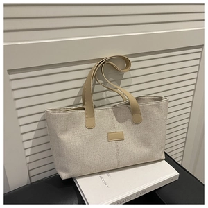 Close-up of beige canvas tote bag with brown leather handles on a white book prop