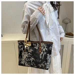 Detail of black tote bag with white bamboo print, brown handles and decorative silk scarf