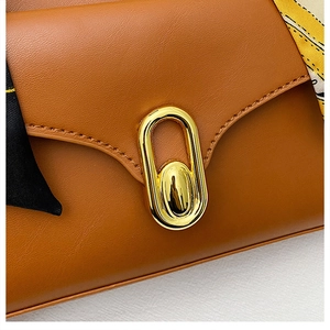 Détail du sac à main en cuir caramel avec boucle dorée et poignée en foulard de soie