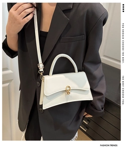 Weiße trapezförmige Handtasche mit goldenem Verschluss über einem schwarzen Blazer