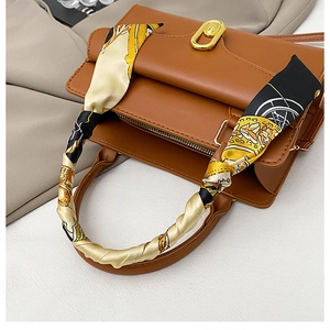 Détail d'un sac à main marron avec poignée enveloppée d'un foulard en soie et fermoir doré