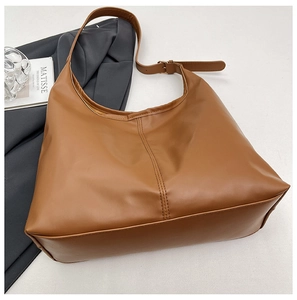 Detail of a large brown leather tote bag featuring vertical stitching and adjustable strap