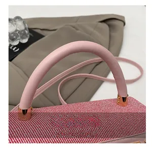 Détail des anses en cuir rose et anneaux dorés sur le sac à main tissé rouge et blanc